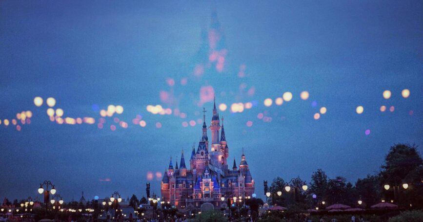 A brightly lit castle, likely at a theme park, stands against a twilight sky with glowing lights and reflections, evoking the magic and wonder often described by creativity speaker Duncan Wardle.