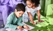 Two young children are drawing together at a table, surrounded by art supplies. One is focused on coloring, while the other observes and holds a green marker, ready to inspire creativity through their shared artwork.